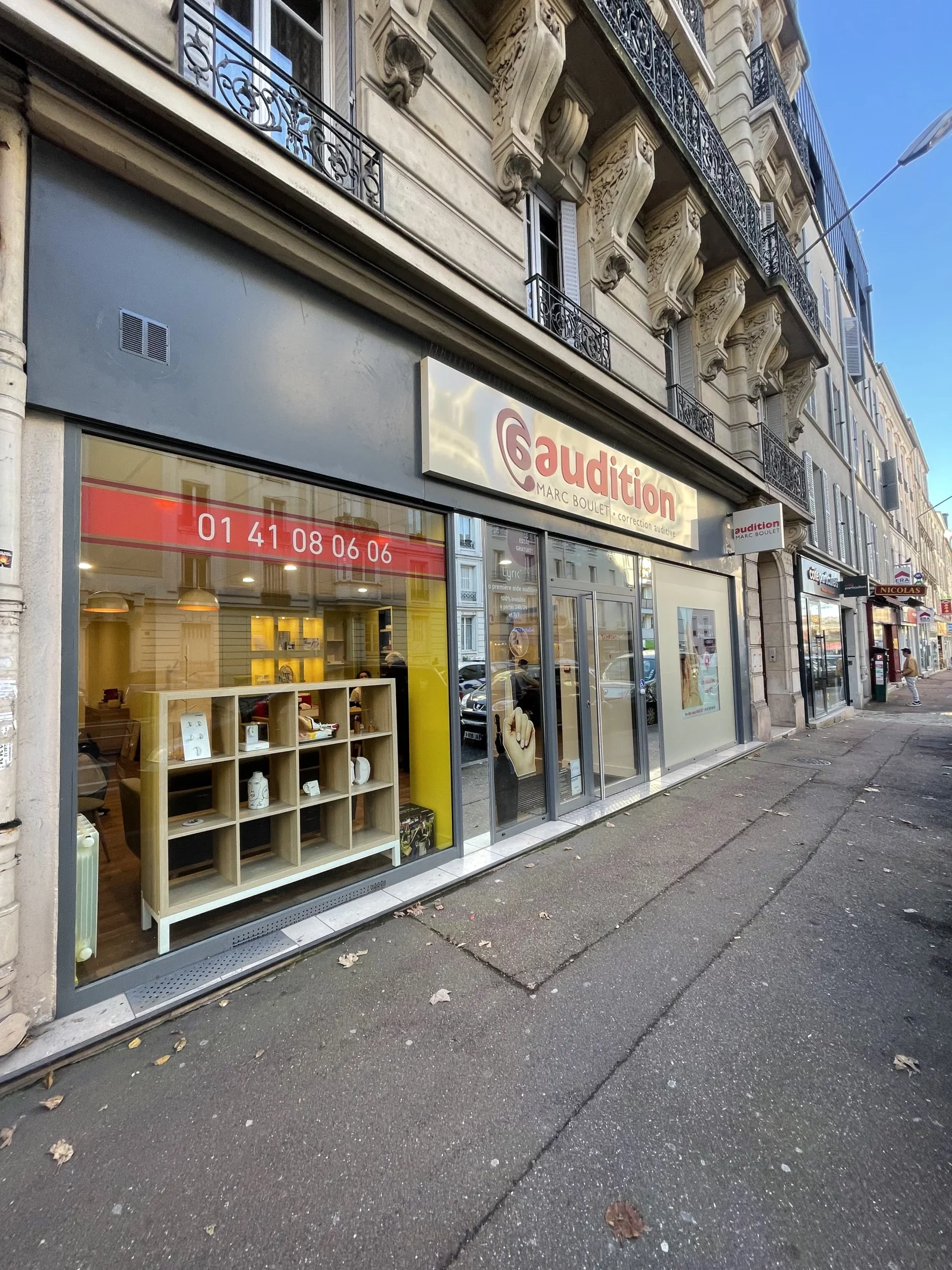 Une façade de boutique d'audition à Paris, avec vitrine moderne, affichage lumineux et espace intérieur visible, spécialisée dans les services d'audition et appareils auditifs, située dans un quartier.